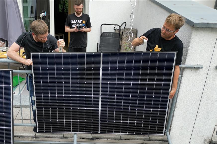 Die Smart-Home-Fox Experten heben das Solarmodul des Solakon Balkonkraftwerks über das Geländer am Balkon während der Installation im Test.